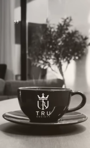 A black coffee cup and saucer with the TRU Society mark, in black and white